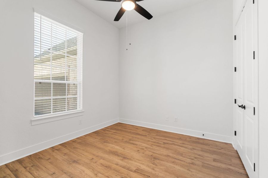 A well-lit bedroom features durable wood flooring and a modern ceiling fan for comfort.
