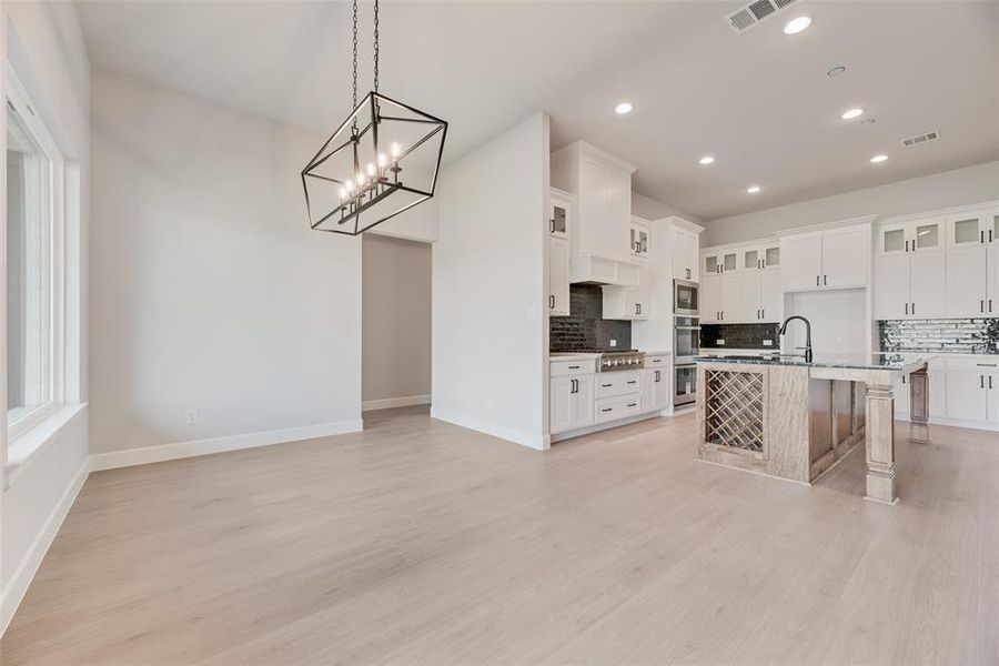 Kitchen featuring tasteful backsplash, a breakfast bar, glass insert cabinets, light wood-style flooring, and recessed lighting