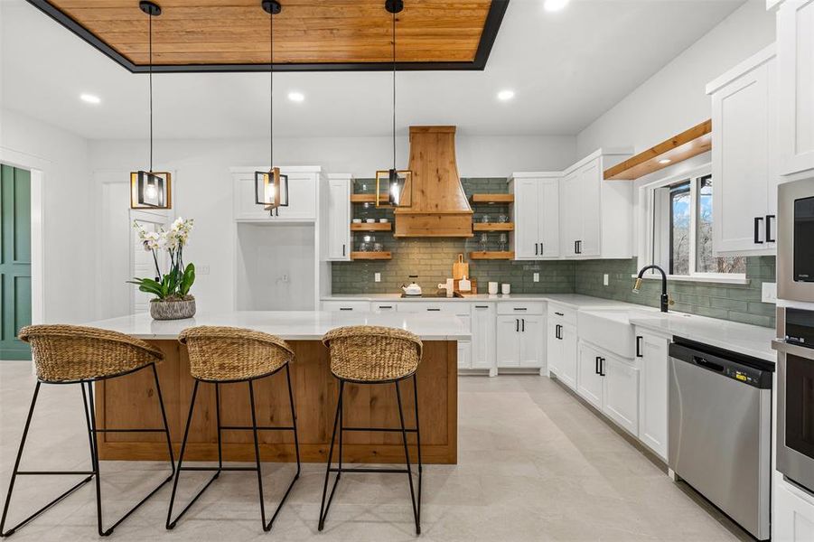 Kitchen featuring white cabinets, appliances with stainless steel finishes, a center island, hanging light fixtures, and light countertops