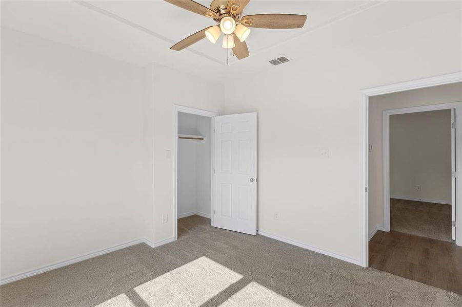 Unfurnished bedroom with carpet flooring, a spacious closet, and a ceiling fan Unfurnished bedroom with carpet flooring, a spacious closet, and a ceiling fan