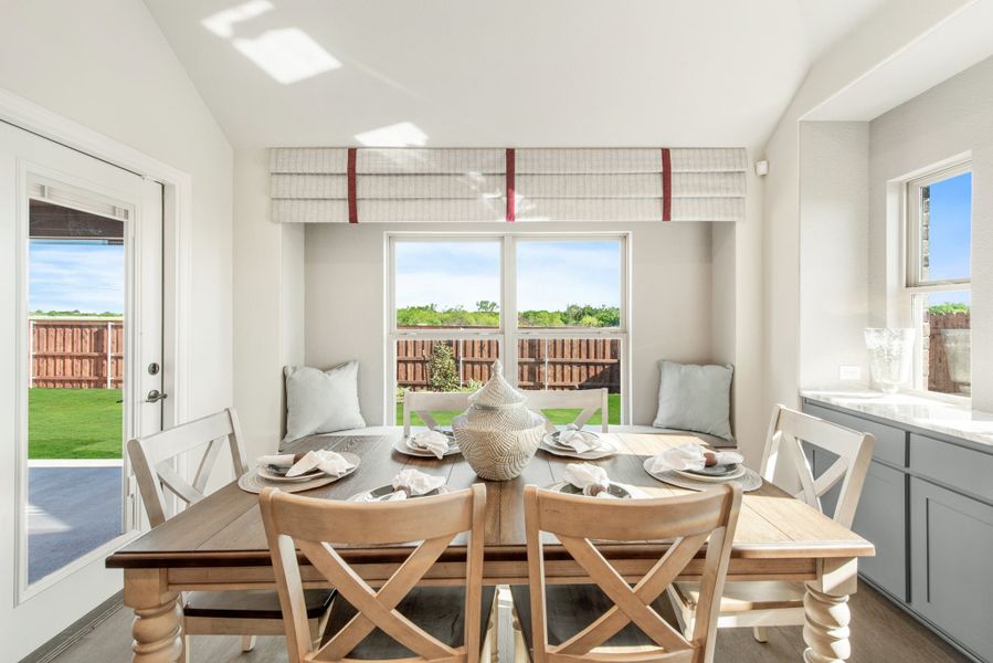Bright dining area with wood table, cross-back chairs, window bench seat, and backyard views through large windows