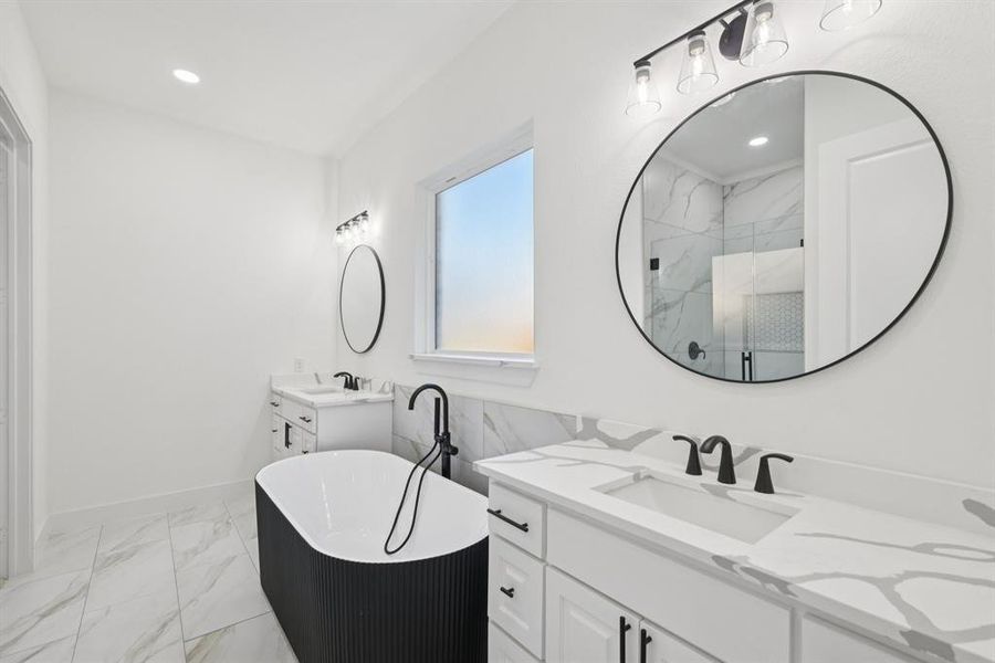Full bathroom featuring light marble finish floors, a freestanding bath, two vanities, a marble finish shower, and recessed lighting