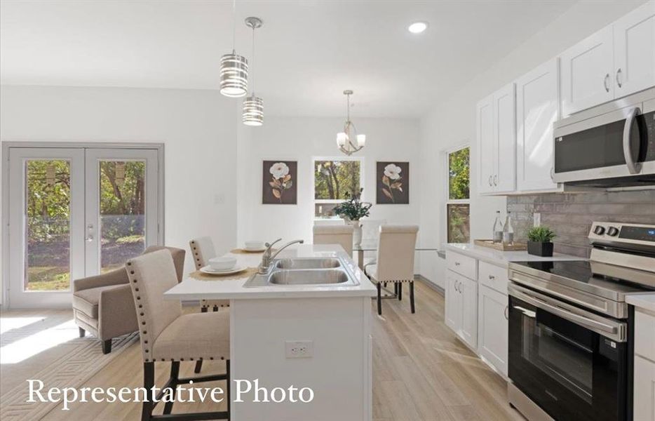 Kitchen with white cabinetry, sink, an island with sink, a kitchen bar, and appliances with stainless steel finishes