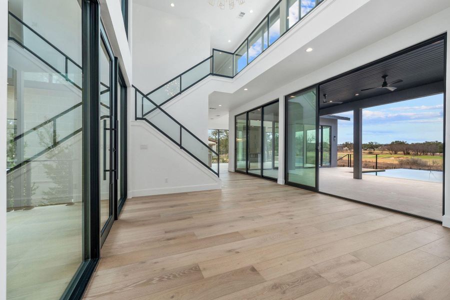 Empty room featuring light wood-style floors, a high ceiling, and suspended lighting