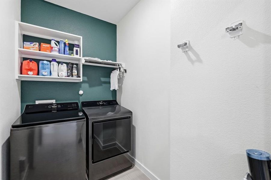 Laundry area featuring modern front-loading appliances, white shelving, and a wall-mounted hanging rod Laundry area featuring modern front-loading appliances, white shelving, and a wall-mounted hanging rod