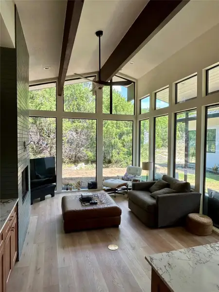 Living area featuring beamed ceiling, light wood finished floors, high vaulted ceiling, plenty of natural light, and a large fireplace Living area featuring beamed ceiling, light wood finished floors, high vaulted ceiling, plenty of natural light, and a large fireplace