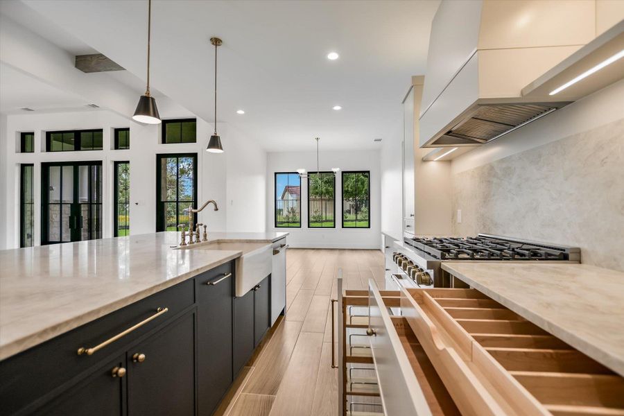 Modern kitchen featuring a large island with an integrated farmhouse sink, pendant lighting, professional-grade gas range, custom hood vent, and light wood-finish flooring