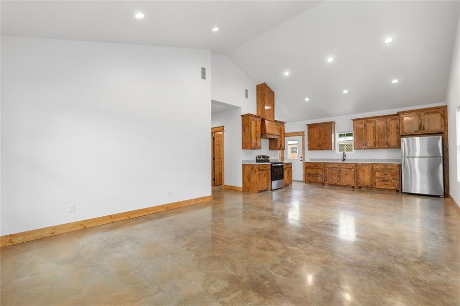 Kitchen with appliances with stainless steel finishes, brown cabinetry, finished concrete flooring, a sink, and high vaulted ceiling Kitchen with appliances with stainless steel finishes, brown cabinetry, finished concrete flooring, a sink, and high vaulted ceiling