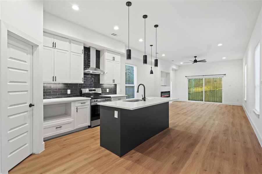 Kitchen with white cabinets, wall chimney exhaust hood, a kitchen island with sink, and stainless steel range