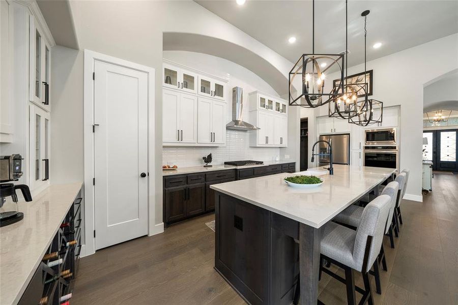 Kitchen featuring appliances with stainless steel finishes, white cabinetry, wall chimney exhaust hood, a center island with sink, and dark hardwood / wood-style floors