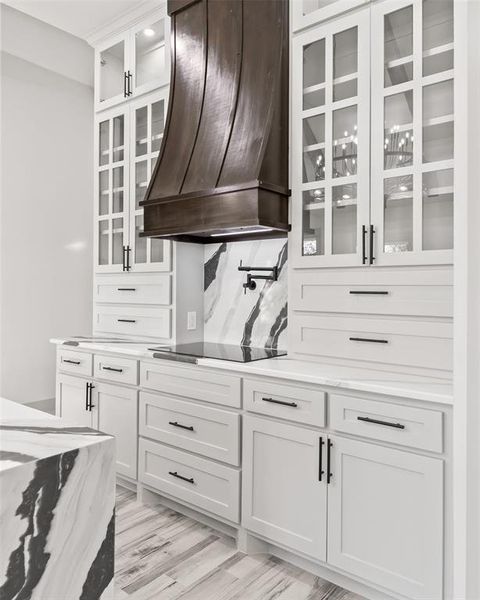 Kitchen featuring premium range hood, glass insert cabinets, white cabinetry, light stone countertops, and tasteful backsplash Kitchen featuring premium range hood, glass insert cabinets, white cabinetry, light stone countertops, and tasteful backsplash