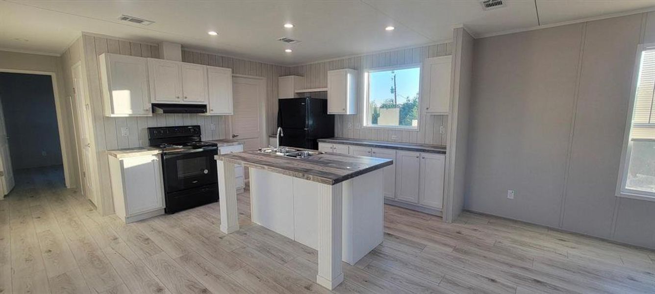 Kitchen featuring black appliances, visible vents, under cabinet range hood, and light wood-type flooring