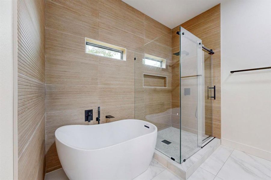 Freestanding soaking tub with matte black fixtures, glass-enclosed shower, and textured tile wall Freestanding soaking tub with matte black fixtures, glass-enclosed shower, and textured tile wall