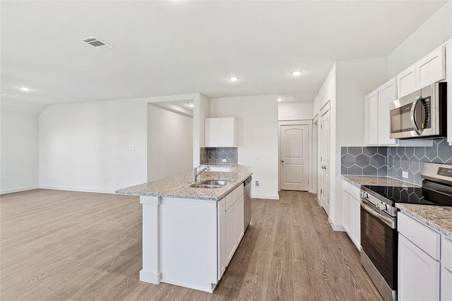 Kitchen featuring white cabinets, a center island with sink, appliances with stainless steel finishes, and light hardwood / wood-style flooring