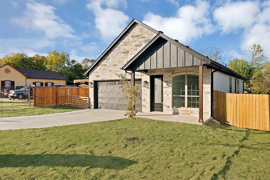 View of front of house featuring board and batten siding, driveway, stone siding, and an attached garage