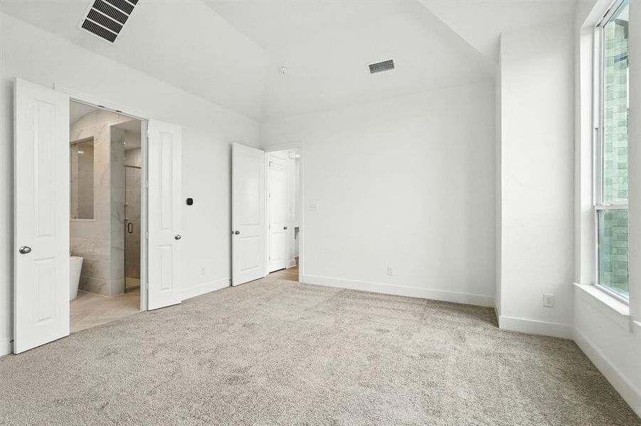 Unfurnished bedroom featuring multiple windows, light carpet, lofted ceiling, and ensuite bath Unfurnished bedroom featuring multiple windows, light carpet, lofted ceiling, and ensuite bath