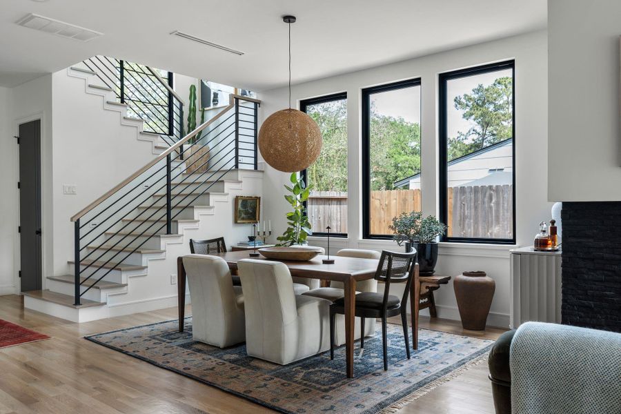 The dining area is framed by oversized windows, hardwood floors, and a new statement light fixture that adds warmth to the modern design.