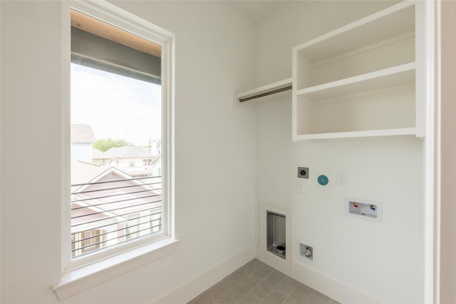 A utility room that earned its square footage. Built-in white shelving stacks vertically above a dedicated hang rod, two windows pull in daylight from adjacent walls, and hookups are tucked neatly into the casework, the kind of room that makes laundry day feel less like a chore.