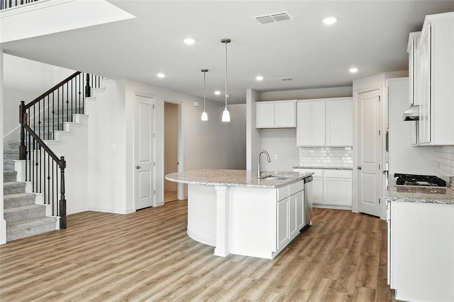 Kitchen with decorative backsplash, light wood-type flooring, a center island with sink, light stone countertops, and white cabinets Kitchen with decorative backsplash, light wood-type flooring, a center island with sink, light stone countertops, and white cabinets