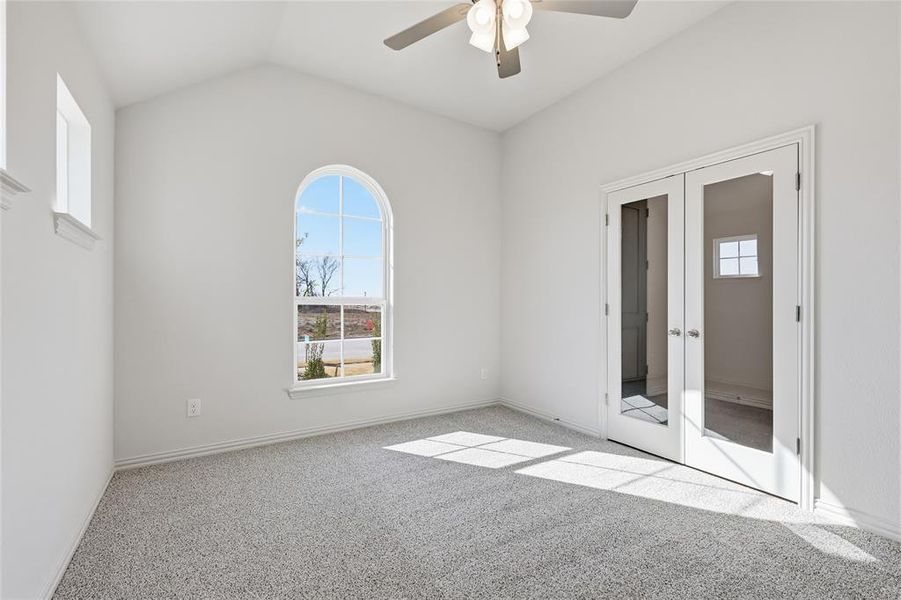 Carpeted empty room with french doors, plenty of natural light, lofted ceiling, and a ceiling fan