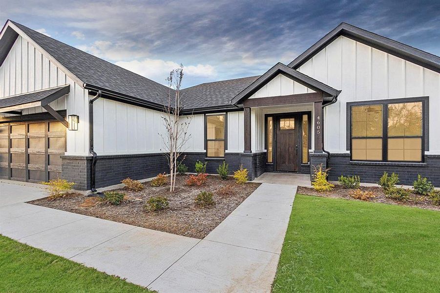 Modern farmhouse with board and batten siding, a front lawn, roof with shingles, and an attached garage