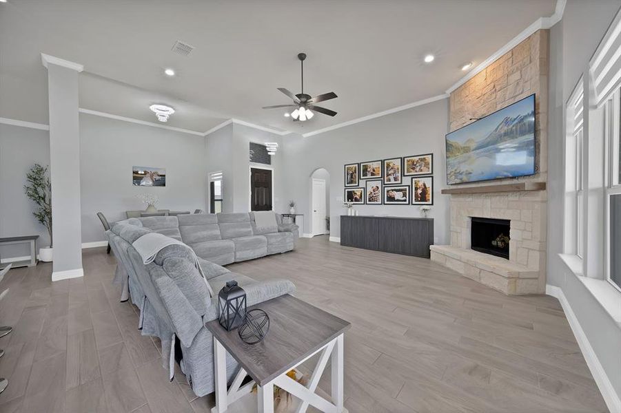 Living room with arched walkways, ornamental molding, ceiling fan, a fireplace, and baseboards Living room with arched walkways, ornamental molding, ceiling fan, a fireplace, and baseboards