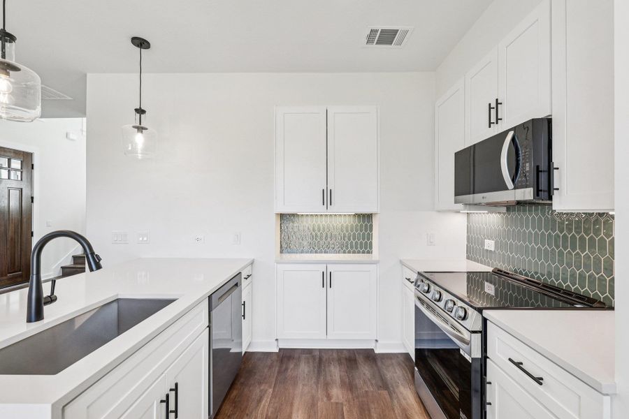 Kitchen with stainless steel appliances, backsplash, white cabinetry, hanging light fixtures, and dark wood finished floors