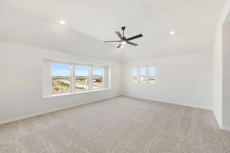 Empty bedroom with vaulted ceiling, ceiling fan, carpet flooring, and large windows with neighborhood views