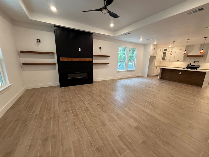 Unfurnished living room with a ceiling fan, a raised ceiling, recessed lighting, light wood finished floors, and a fireplace Unfurnished living room with a ceiling fan, a raised ceiling, recessed lighting, light wood finished floors, and a fireplace