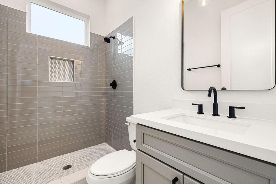 The secondary bathroom boasts elegant light countertops paired with contemporary grey cabinetry, creating a refined and airy atmosphere. The oversized walk-in shower, with its custom tile surround, offers a spa-like experience, while the decorative mirror adds a touch of sophistication. The sleek fixtures and modern finishes complement the tile floors, enhancing the bathroom’s sleek design. The secondary bathroom boasts elegant light countertops paired with contemporary grey cabinetry, creating a refined and airy atmosphere. The oversized walk-in shower, with its custom tile surround, offers a spa-like experience, while the decorative mirror adds a touch of sophistication. The sleek fixtures and modern finishes complement the tile floors, enhancing the bathroom’s sleek design.