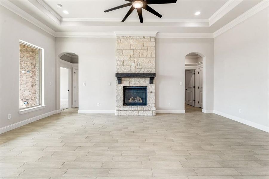 Unfurnished living room featuring arched walkways, light wood-type flooring, a stone fireplace, a tray ceiling, and recessed lighting