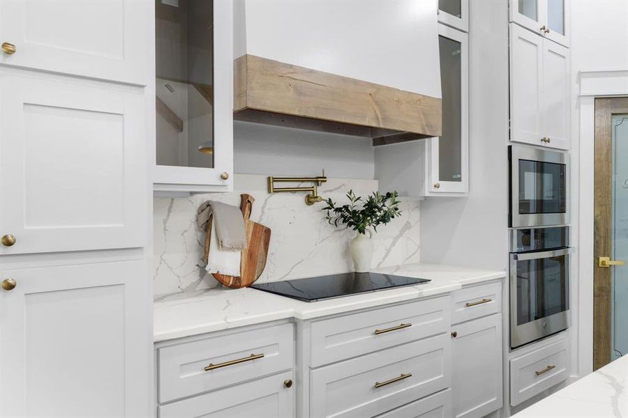 Kitchen featuring tasteful backsplash, white cabinetry, stainless steel appliances, range hood, and light stone counters