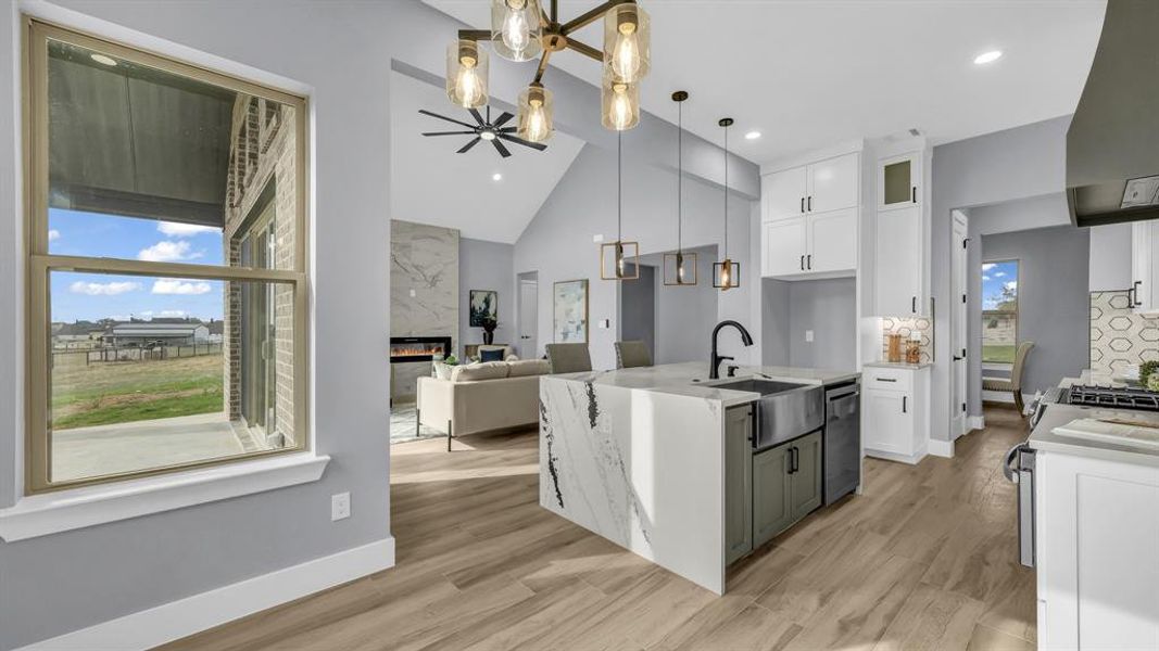 Kitchen with a kitchen island with sink, light stone countertops, a high end fireplace, white cabinetry, and healthy amount of natural light