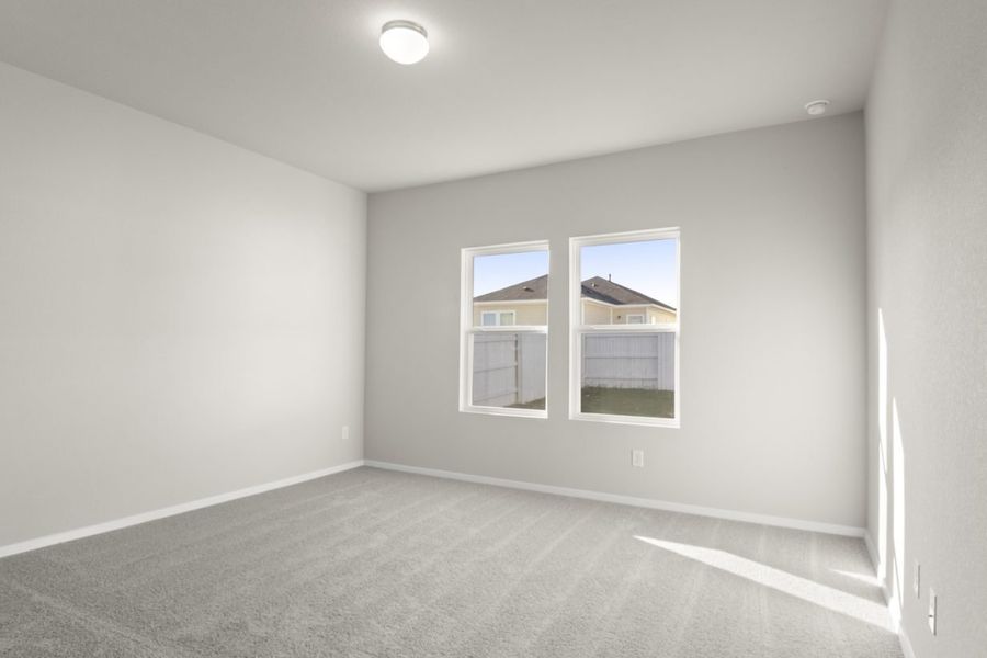 Image of primary bedroom with tan carpeting and light grey painted walls with two windows