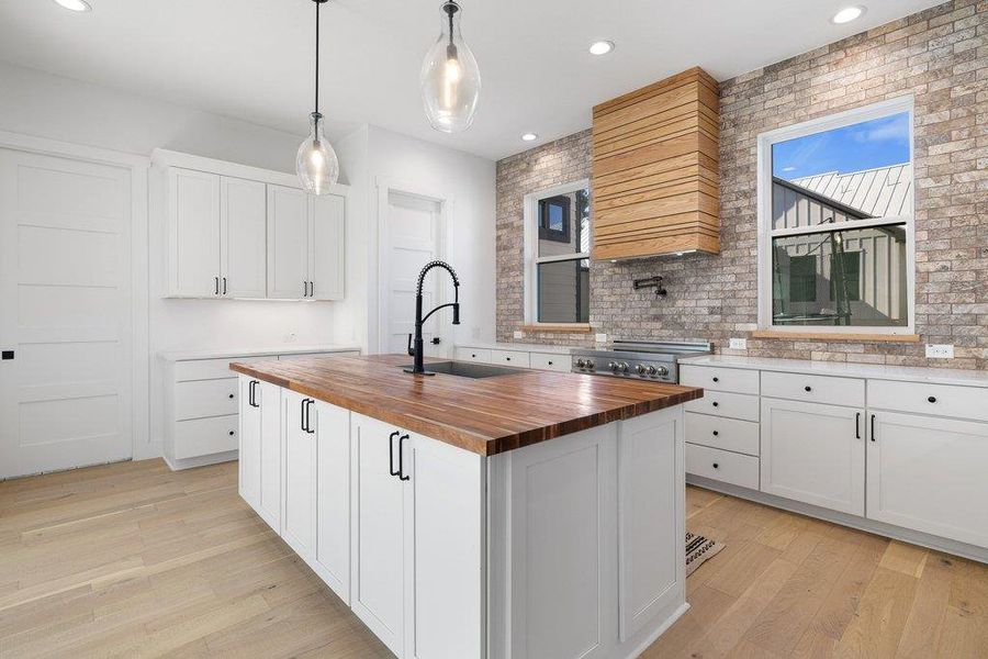 Kitchen featuring butcher block counters, an island with sink, decorative light fixtures, and white cabinetry