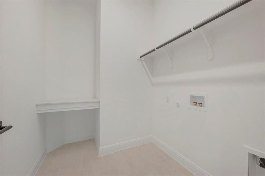Dedicated laundry area featuring a built-in hanging rod, wall-mounted shelf supports, washer/dryer hookups, and light-colored tile flooring