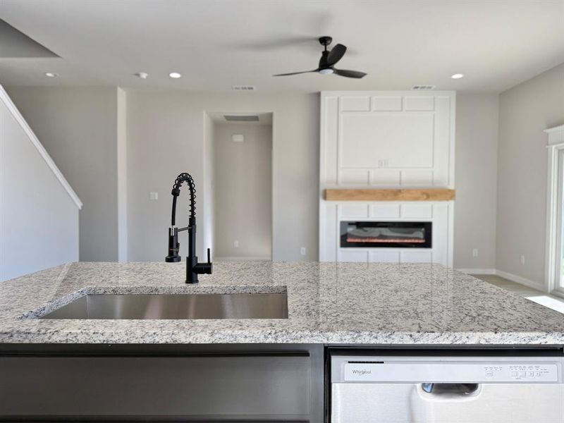 Kitchen with light stone countertops, ceiling fan, sink, and dishwashing machine