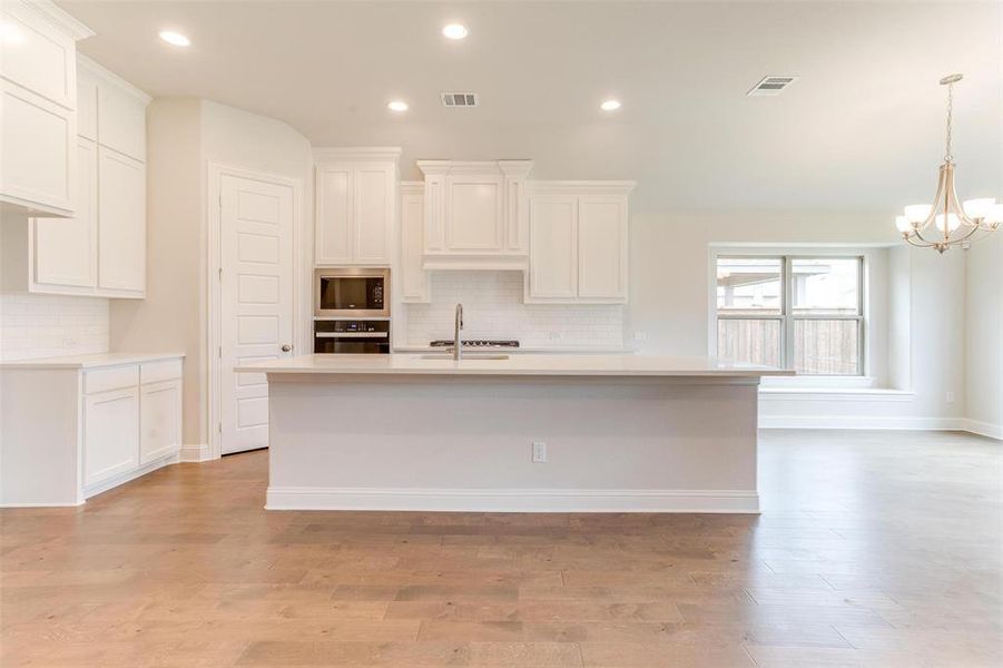 Kitchen featuring light hardwood / wood-style floors, a kitchen island with sink, black appliances, and backsplash