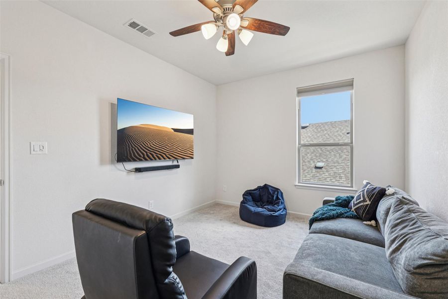 This inviting room features a ceiling fan, a window, and light-colored carpeting