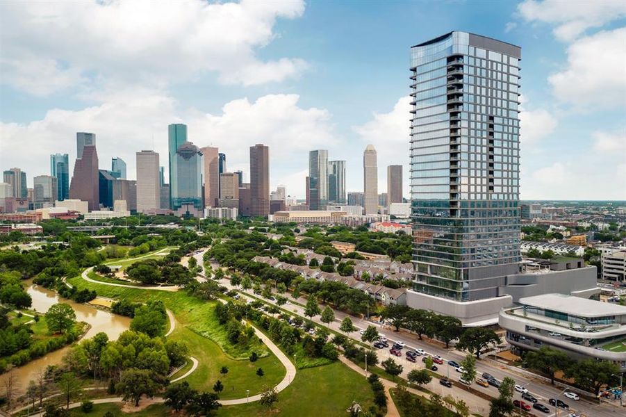 The Residences at The Allen, Houston’s premiere Luxury Condo Hotel Tower on Allen Parkway, Houston, stands gracefully against the city skyline. Its modern design and glass windows exude sophistication, while a warm glow from the setting sun highlights its elegance. Private balconies with lush greenery offer panoramic views of downtown Houston and Buffalo Bayou Park. This building embodies luxury living, with exceptional amenities and breathtaking vistas.