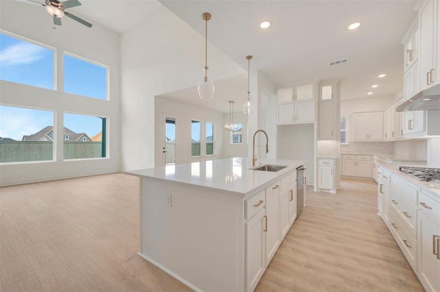 Open-concept living space featuring a kitchen island with sink and stainless steel dishwasher, white cabinetry with gold-finish hardware, recessed lighting, and wood-finish flooring