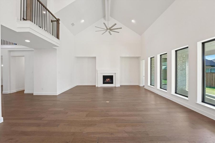 Unfurnished living room featuring beamed ceiling, high vaulted ceiling, a lit fireplace, dark wood-type flooring, and a ceiling fan
