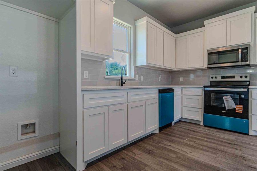Kitchen featuring electric range, stainless steel microwave, dark wood-style flooring, light countertops, and white cabinetry Kitchen featuring electric range, stainless steel microwave, dark wood-style flooring, light countertops, and white cabinetry