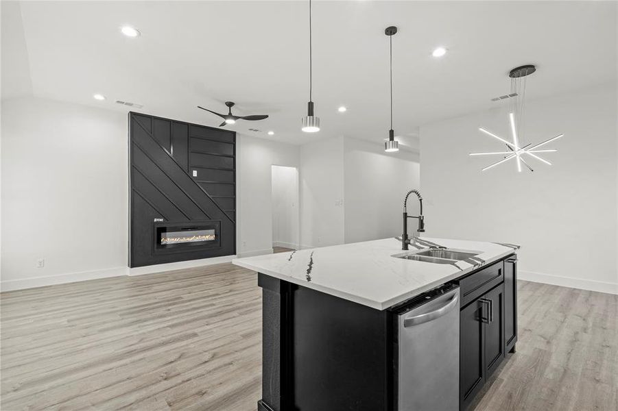 Kitchen featuring sink, stainless steel dishwasher, pendant lighting, a kitchen island with sink, and a fireplace