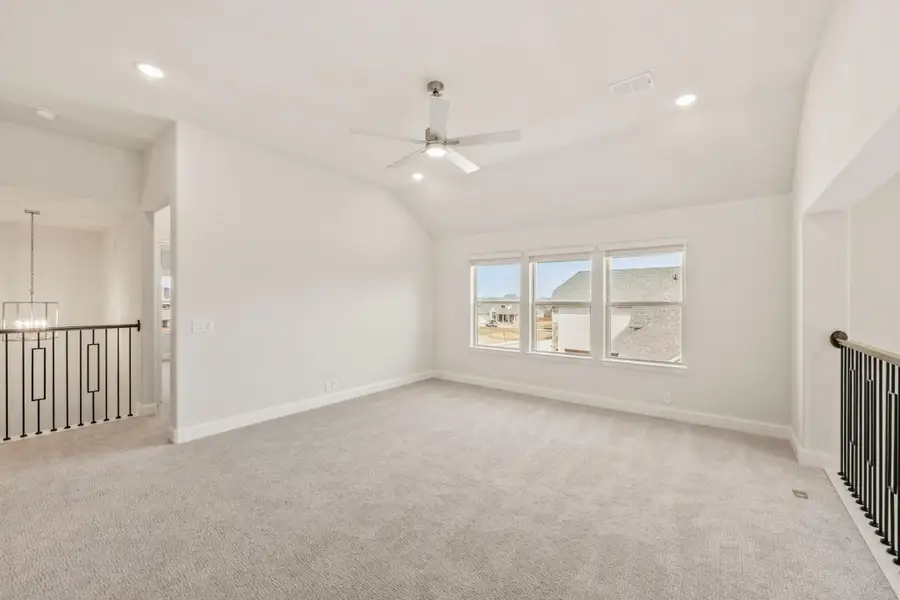 Empty upstairs bonus room with vaulted ceiling, ceiling fan, carpet, and triple window overlooking neighborhood