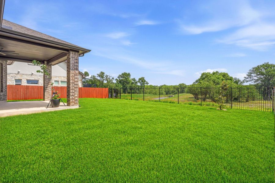 Spacious backyard featuring a covered patio with brick columns, concrete flooring, and a ceiling fan