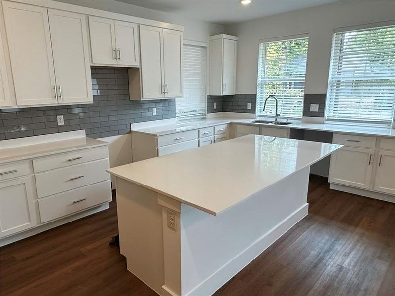 Kitchen featuring white cabinets, a center island, decorative backsplash, dark wood-style flooring, and light stone counters