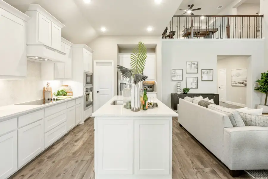 Open-concept kitchen with white cabinets, large island, and living area with second-floor loft visible above