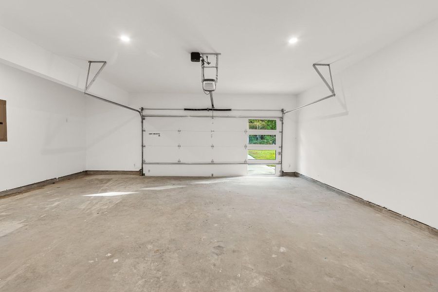 This is a spacious, clean garage with a concrete floor, white walls, and a modern automatic door. It features ample natural light from windows at the back, offering plenty of room for vehicles or storage. This is a spacious, clean garage with a concrete floor, white walls, and a modern automatic door. It features ample natural light from windows at the back, offering plenty of room for vehicles or storage.
