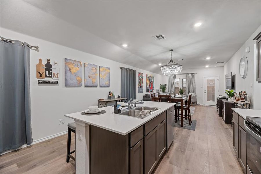 Kitchen with light wood-style flooring, dark brown cabinets, a kitchen island with sink, a breakfast bar, and a chandelier